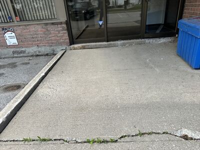 Settled commercial concrete walkway outside a storefront at an Ajax plaza before concrete leveling