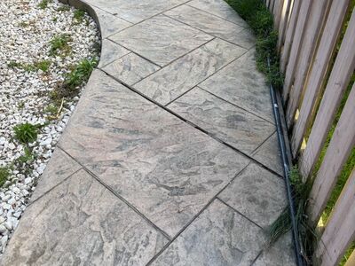 Settled stamped concrete side walkway curving along a fence line in Mississauga, Ontario before polyurethane concrete leveling