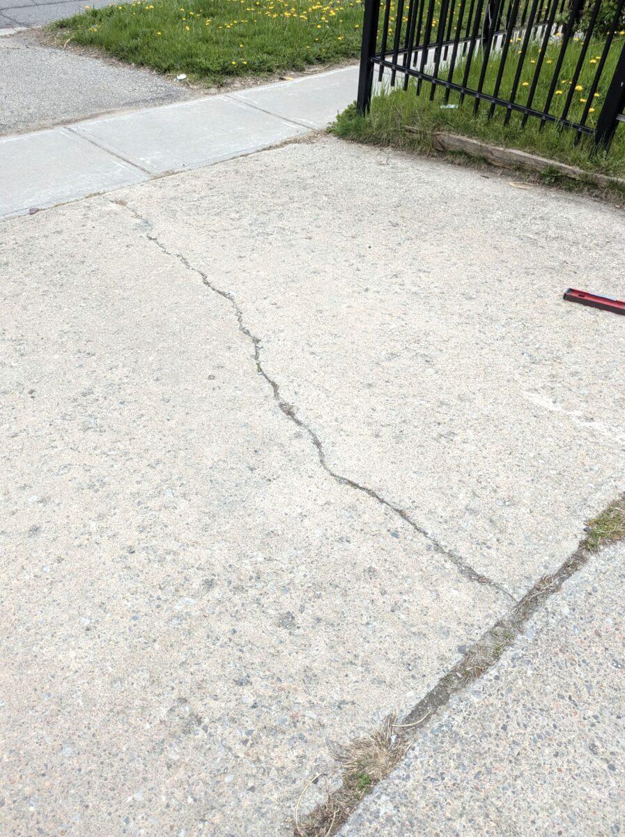 Cracked, settled concrete driveway in Toronto before repair, showing a jagged fracture and displaced slab